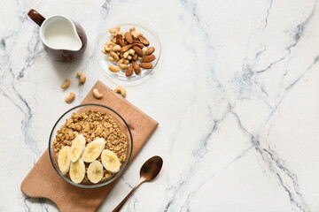 Wooden cutting board, nuts, bowl with tasty granola and banana on marble background