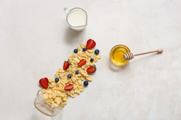 Overturned bowl with scattered cornflakes and berries on light background
