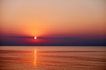 Obraz premium A serene sunset over a calm ocean with birds flying in the sky. The sun dips below the horizon, casting a warm glow over the landscape.