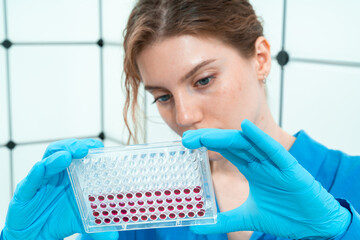 female laboratory assistant in genetics laboratory working with multi pipette and ninety-six well...