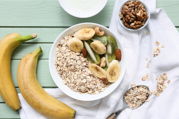 Napkin, fruits and bowl with raw oatmeal on green wooden background, closeup
