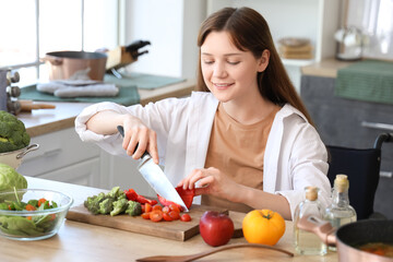 Young woman in wheelchair cutting bell pepper at home