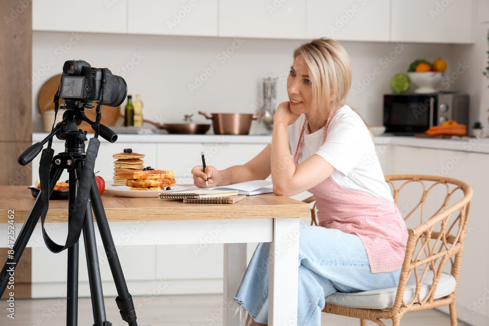 Sticker female food blogger writing on notebook while recording video in kitchen