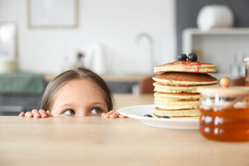 Cute little girl and pancakes with honey on table in kitchen, closeup