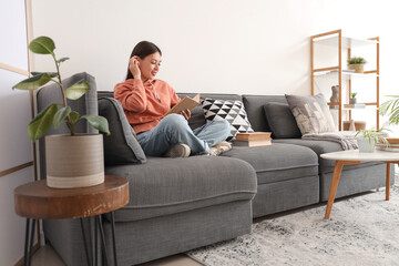 Beautiful young woman reading on sofa at home