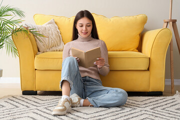 Beautiful young woman reading book and sitting on floor at home