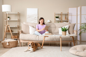 Young woman reading book and cute Beagle dog lying on floor in living room