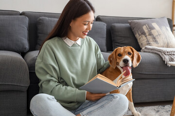 Young woman reading book and sitting with cute Beagle dog on floor in living room