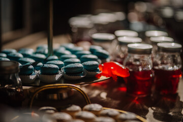 Dobele, Latvia - June 7, 2024 - Close-up of a dessert table with blue macarons on a tray, red jelly, and jars of red liquid in the background.
