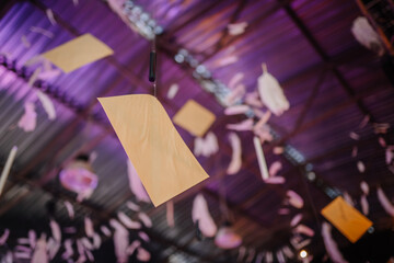 Dobele, Latvia - June 7, 2024 - Close-up of suspended paper and feather decorations hanging from a ceiling with purple lighting, creating a whimsical and festive atmosphere. Copy space.