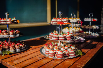 Dobele, Latvia - June 7, 2024 - Tiered trays of assorted desserts, including cakes and cupcakes, displayed on a wooden table with a dark blue background. Copy space.