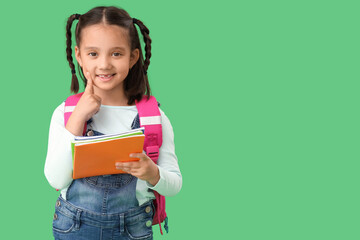Cute little happy Asian girl with backpack and notebooks on green background. End of school year
