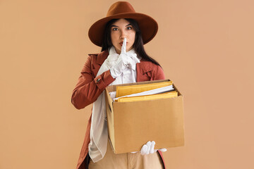 Female spy with box of files showing silence gesture on beige background