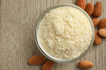 Fresh almond flour in bowl and nuts on wooden table, top view. Space for text