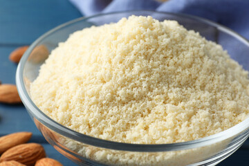 Fresh almond flour in bowl and nuts on blue table, closeup