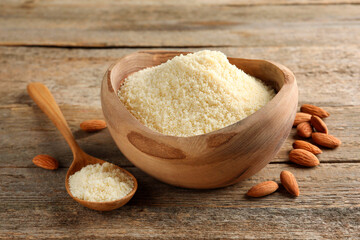 Fresh almond flour in bowl, spoon and nuts on wooden table, closeup