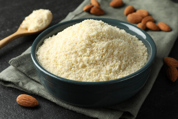 Fresh almond flour in bowl on dark textured table, closeup