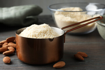 Fresh almond flour in scoop and nuts on wooden table, closeup