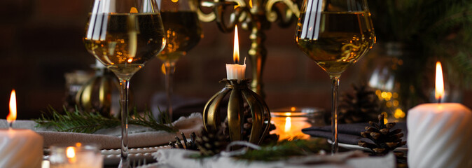 Banner. Beautiful table setting for family Christmas dinner at home. Cozy atmosphere, candlelight. Wine glasses, vintage chandelier, elegant interior. Fir tree branches, wooden furniture, dark, bokeh