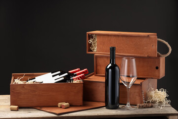 Boxes with wine bottles, corks and glass on wooden table against black background