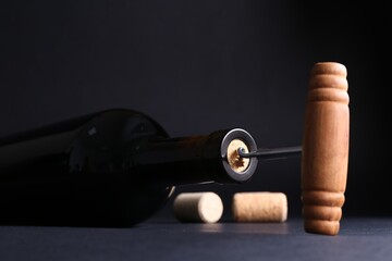 Wine bottle with corkscrew on dark background, closeup