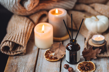 Home comfort, coziness, aromatherapy. Cozy interior with knitting, burning candles and aroma perfume diffuser in the living room. Fall scent, sweet pumpkin pie fragrance, dry leaves, autumn mood