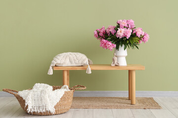 Vase with peonies flowers and pillow on bench in stylish living room