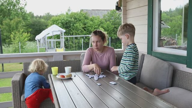 Mother and Sons Playing Dominoes on a Summer Terrace