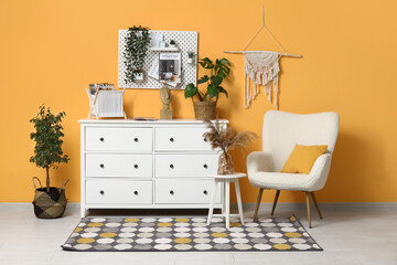 Stylish living room with white chest of drawers, houseplant, soft armchair and pegboard