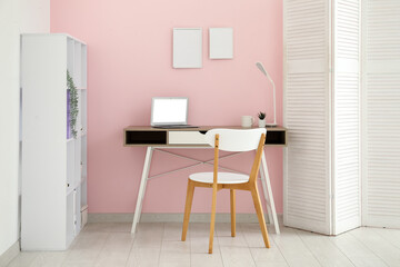 Interior of stylish office with workplace, laptop, chair and shelving unit