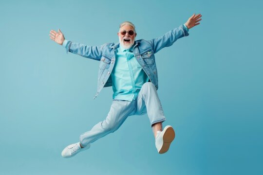 active senior guy in light blue trendy casual outfit dancing and jumping on monochrome color minimal background with copy space. Banking app, retirement program. 