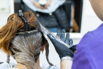 A hairdresser applying dye with a brush to a client's hair in a women's hair salon.