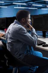 Man working on computer in modern data center, sitting at desk and thinking of solutions. Employee...