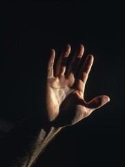 Fototapeta premium A person holds their hand up towards an unknown light source in a dark environment