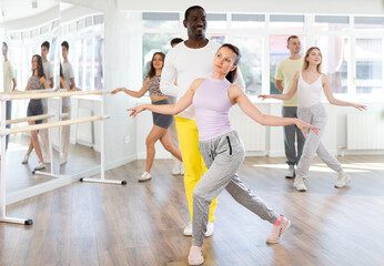 Fototapeta premium Smiling African american man and female partner with multinational group active people training energetic and fast twist or charleston dance movements in modern dance salon