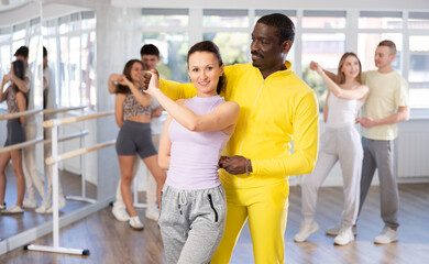 Obraz premium Positive middle-aged woman and Afro-American man engaged in waltz dance in dancehall during workout session