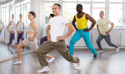 Obraz premium Young happy guy and international dancers preparing their modern dance at light dance studio