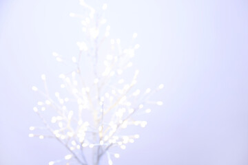 Decorative tree with lights on light background, blurred view. Space for text