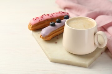 Cup of coffee and delicious eclairs covered with glaze on white wooden table. Space for text