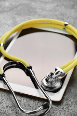 Modern tablet and stethoscope on grey table, closeup