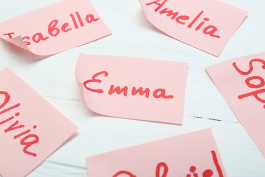 Paper stickers with different names on white wooden table, closeup. Choosing baby's name