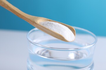 Spoon with baking soda over glass of water on color background, closeup