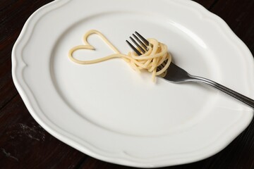 Heart made of tasty spaghetti and fork on wooden table