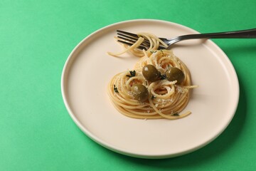 Heart made of tasty spaghetti, fork, olives and cheese on green background