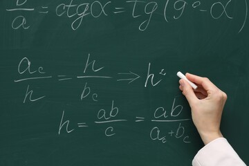 Teacher writing down math equation on green board, closeup