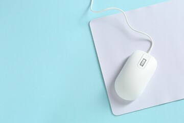 Wired mouse and mousepad on light blue background, top view. Space for text