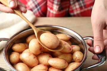 Woman taking raw potato from pot with water at table, closeup