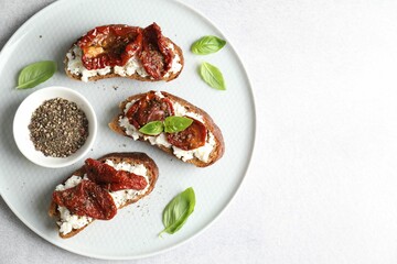 Delicious ricotta bruschettas with sun dried tomatoes, basil and milled pepper on light table, top view. Space for text