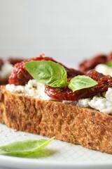 Delicious ricotta bruschetta with sun dried tomatoes and basil on plate, closeup