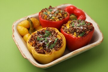 Tasty quinoa stuffed bell peppers with corn in baking dish on light green table
